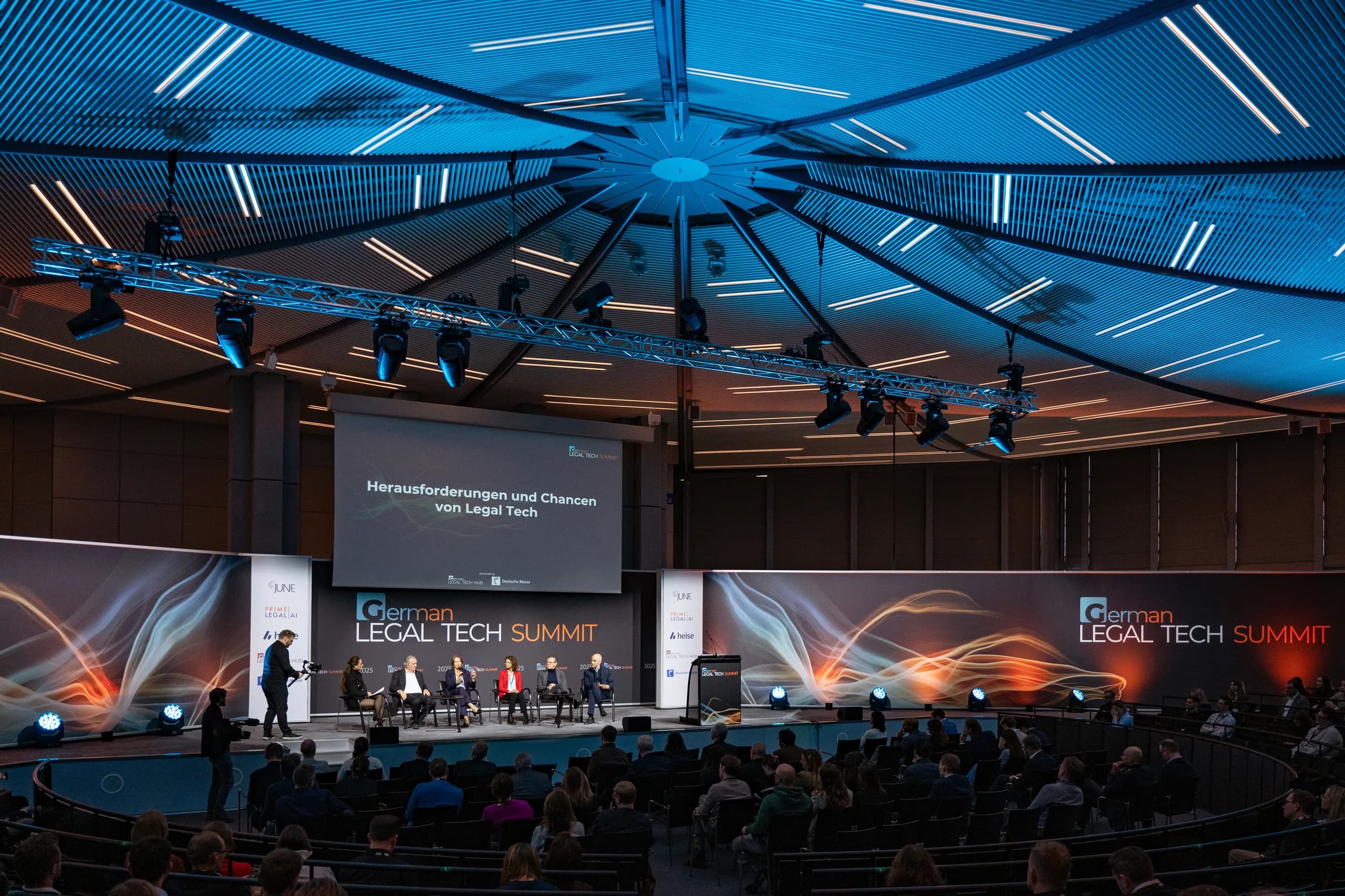 Blick in den vollen Saal unter der beleuchteten Kuppel, auf der Bühne eine Podiumsdiskussion